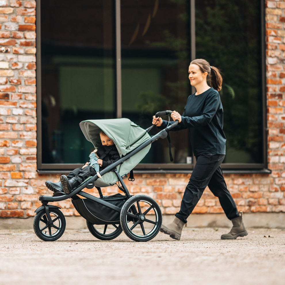 Woman walking with Thule Urban Glide 3 stroller past brick wall.