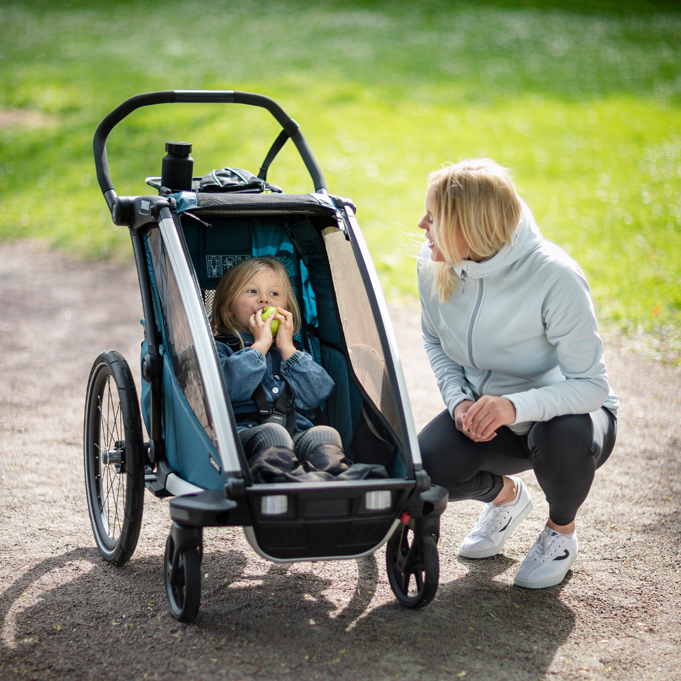 A woman leans down to her child in a bike trailer with a Thule Organizer Sport.