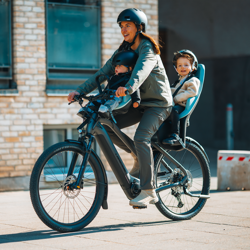 Urban family biking with two children safely seated, one in a front and one in a rear Thule Yepp 2 bike seat.