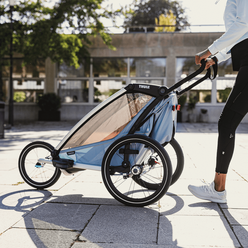 Eine Frau in Sportkleidung läuft mit ihrem Fahrradanhänger für Kinder mit einem Thule-Geländeset.