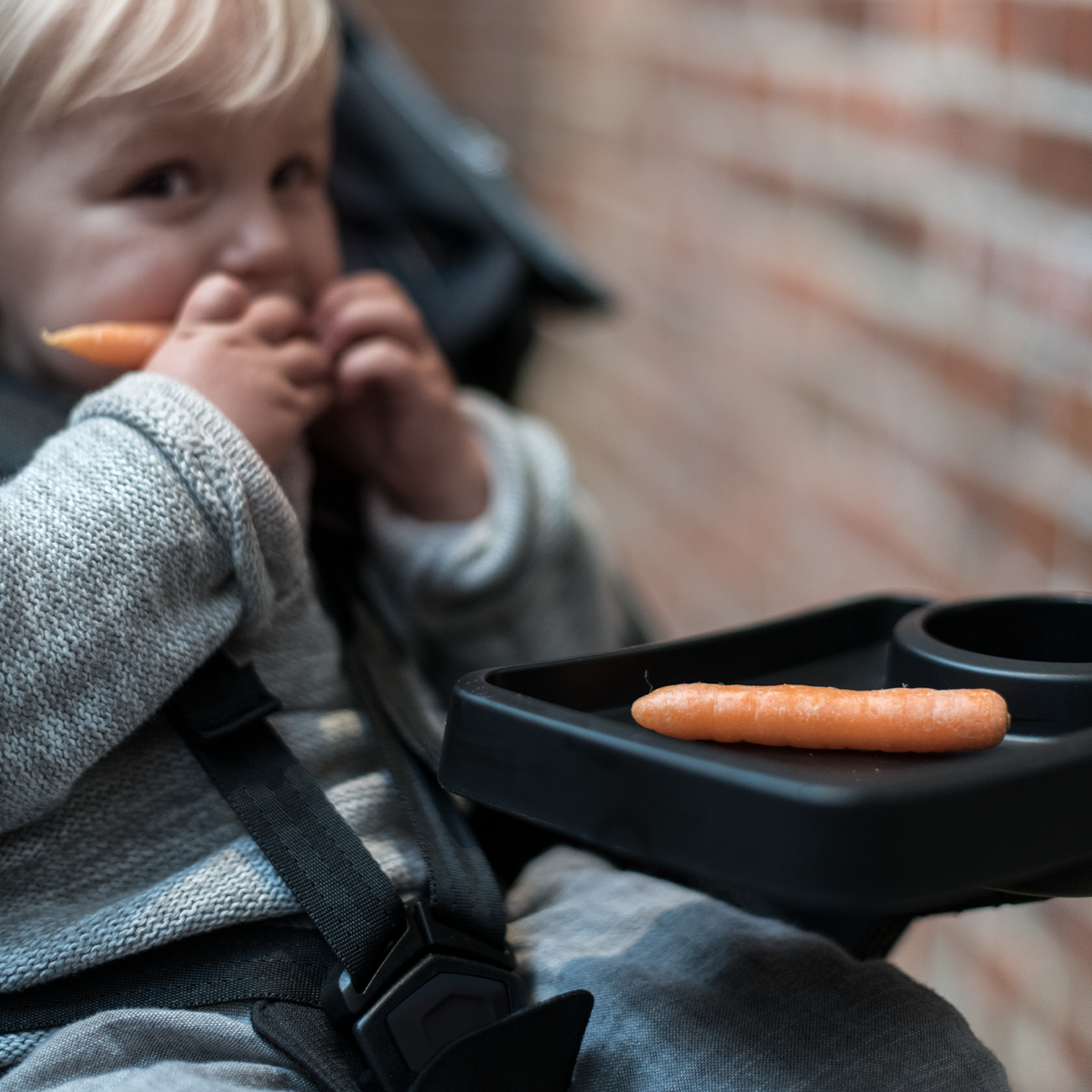 A toddler eats a carrot that is resting on the Thule Urban Glide 2 Snack Tray.