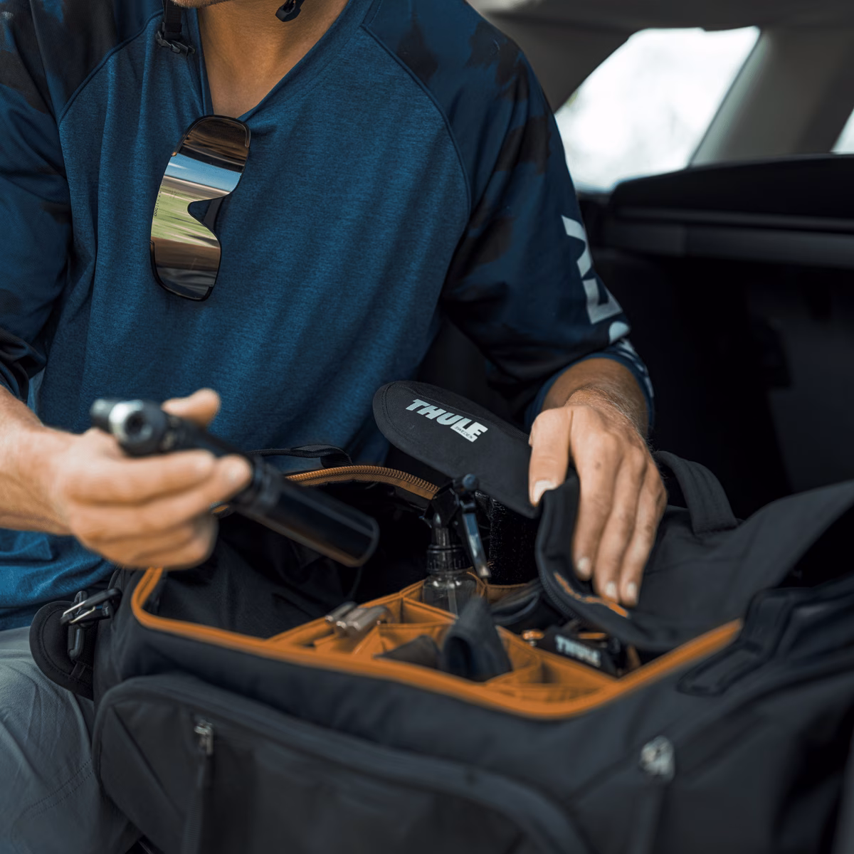 A cyclist has a Thule Roundtrip bike gear duffel in the trunk of his car and rummages for gear.