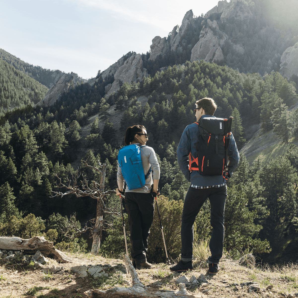 Two people hike in the mountains with Thule AllTrail backpacks.