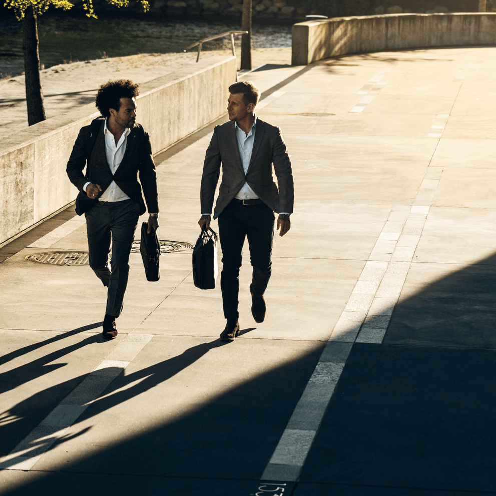 Two men walk down a sunny street in professional clothing carrying Thule Crossover 2 Laptop Bags.