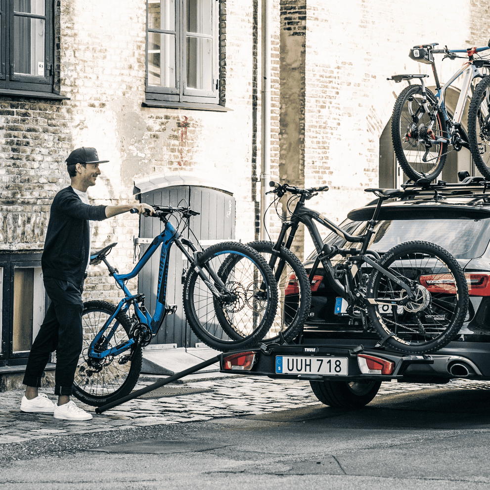 A man rolls his bikes onto the towbar bike rack using the Thule Loading Ramp XT.