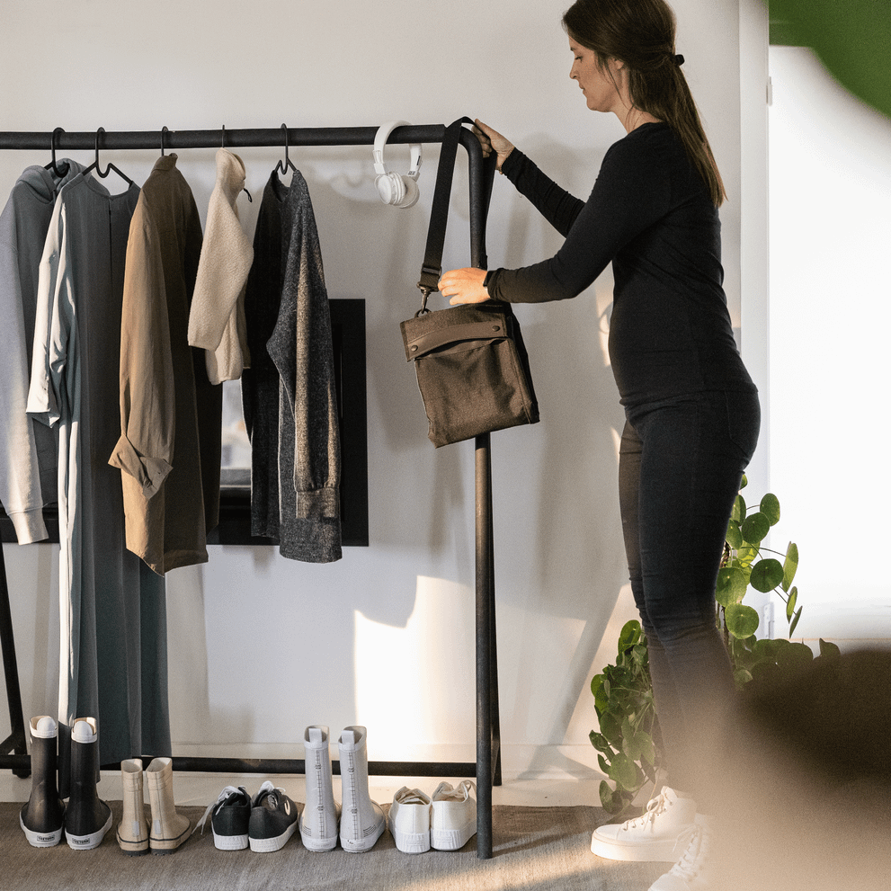 A mother places the Thule Stroller Travel Bag on a clothing rack inside her house.