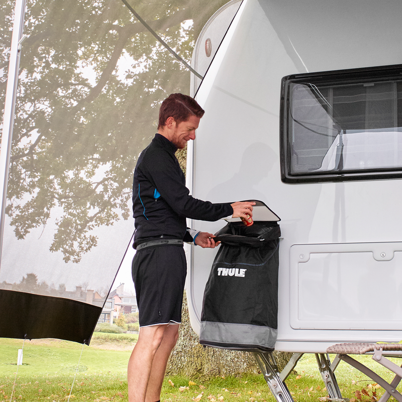 A man throws something into a Thule Trash Bin attached on a caravan.