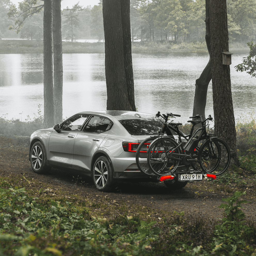 A car is parked next to a lake by the forest with bikes installed on the Thule Epos hitch bike rack.