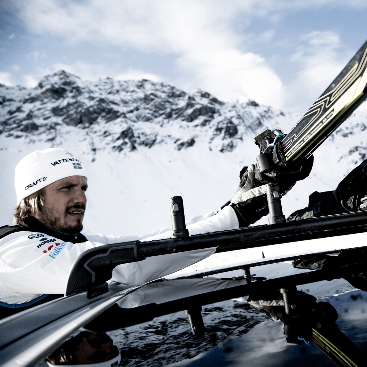 A man is loading his skis on a car roof using Thule SkiClick