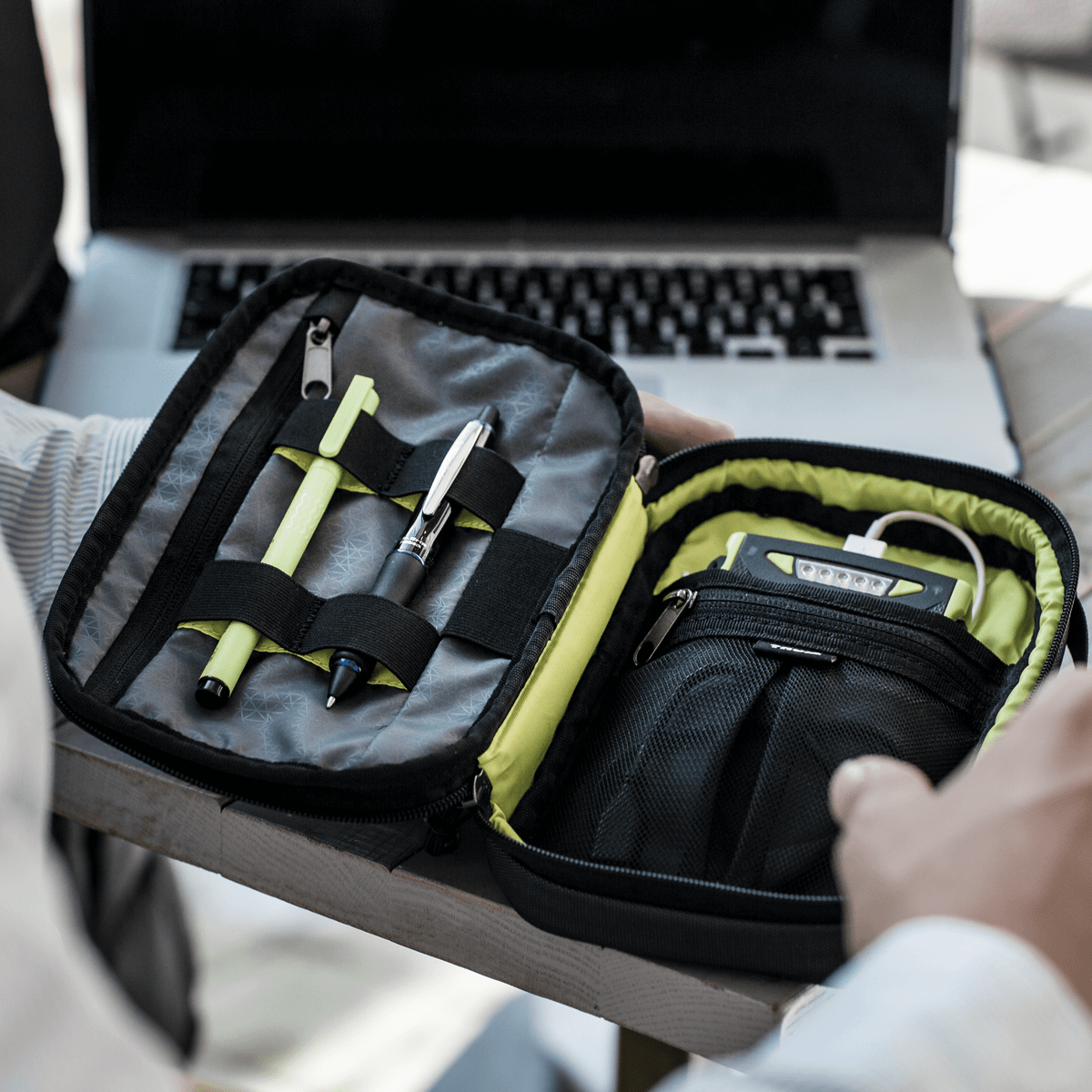 A close-up of a laptop and Thule Subterra PowerShuttle electronics organizer with battery and pens.