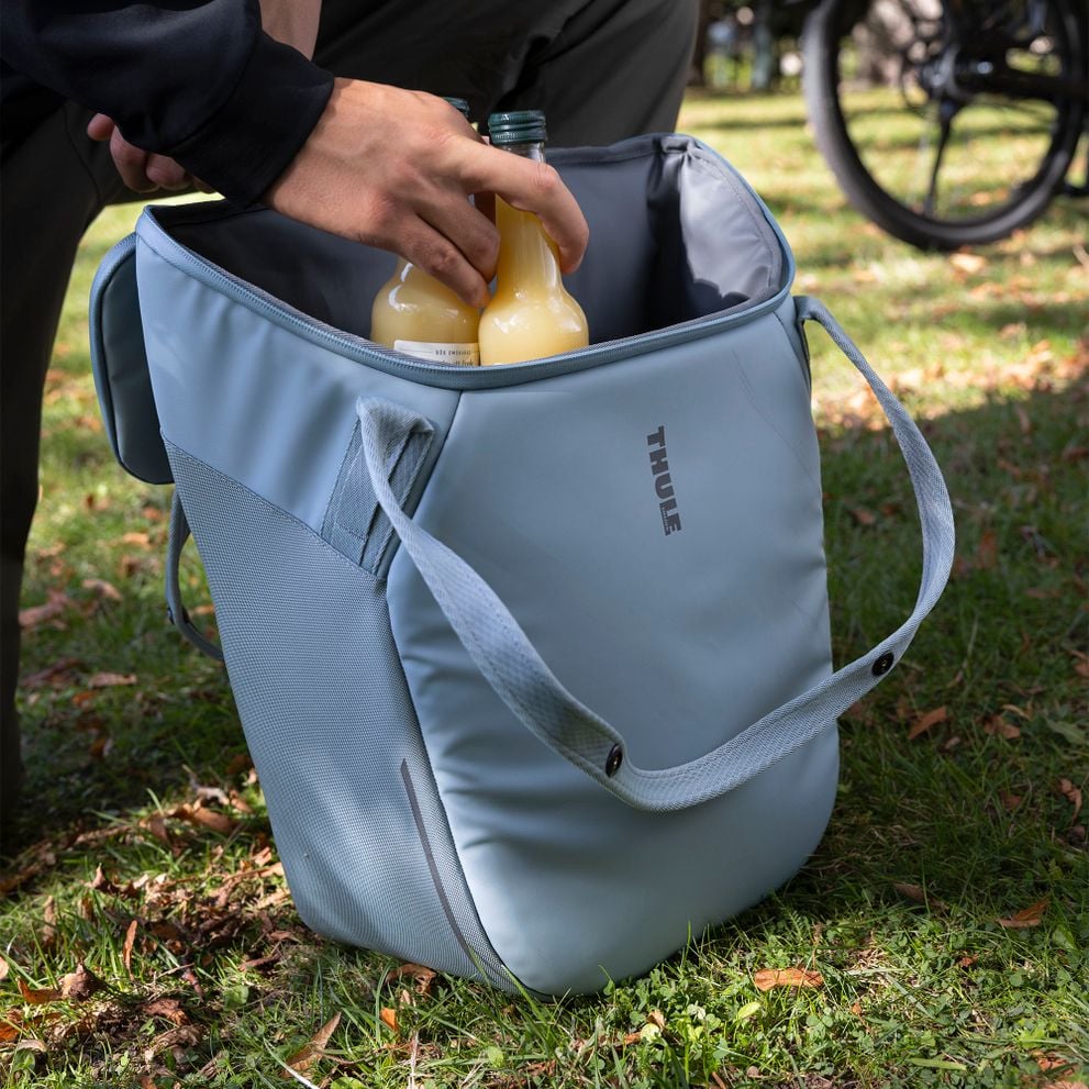 Hand placing bottles into a Thule Chasm bag outdoors.