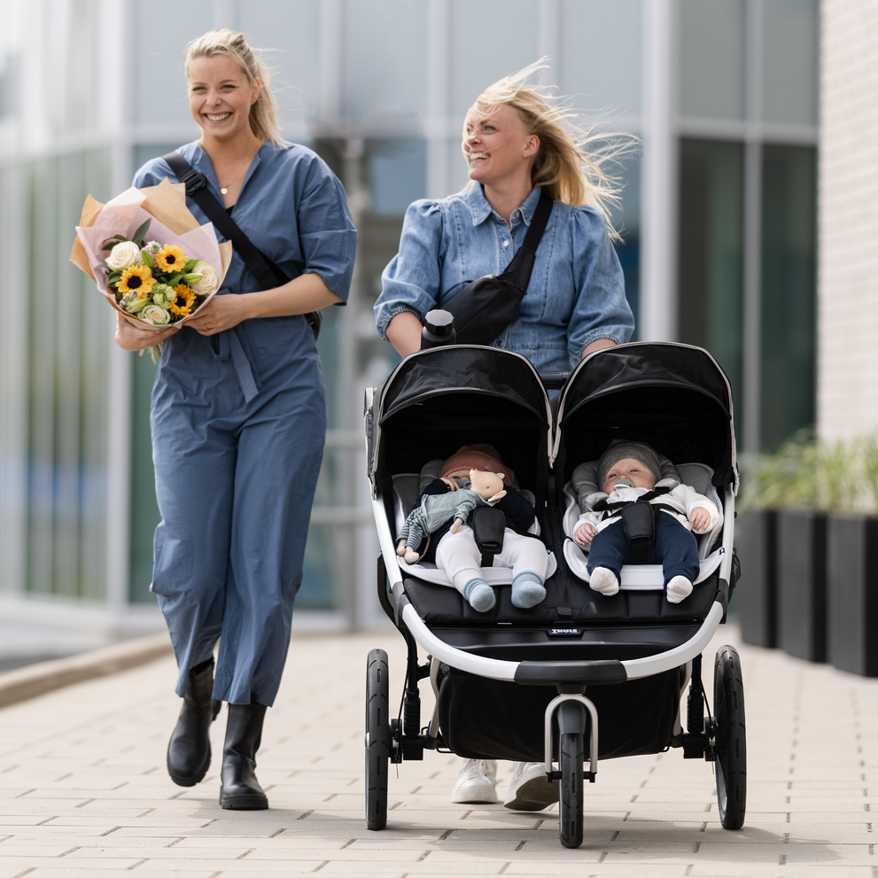 Two mothers walk with their kids nestled in a Thule Newborn Inlay inside a stroller.