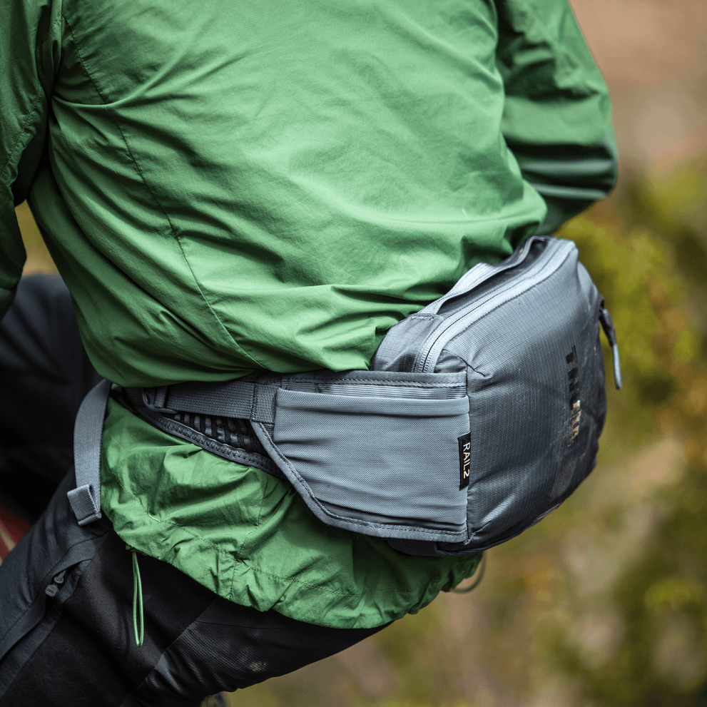 A close-up of a cyclist wearing green carrying a blue Thule Rail 2L hydration Hip Pack.