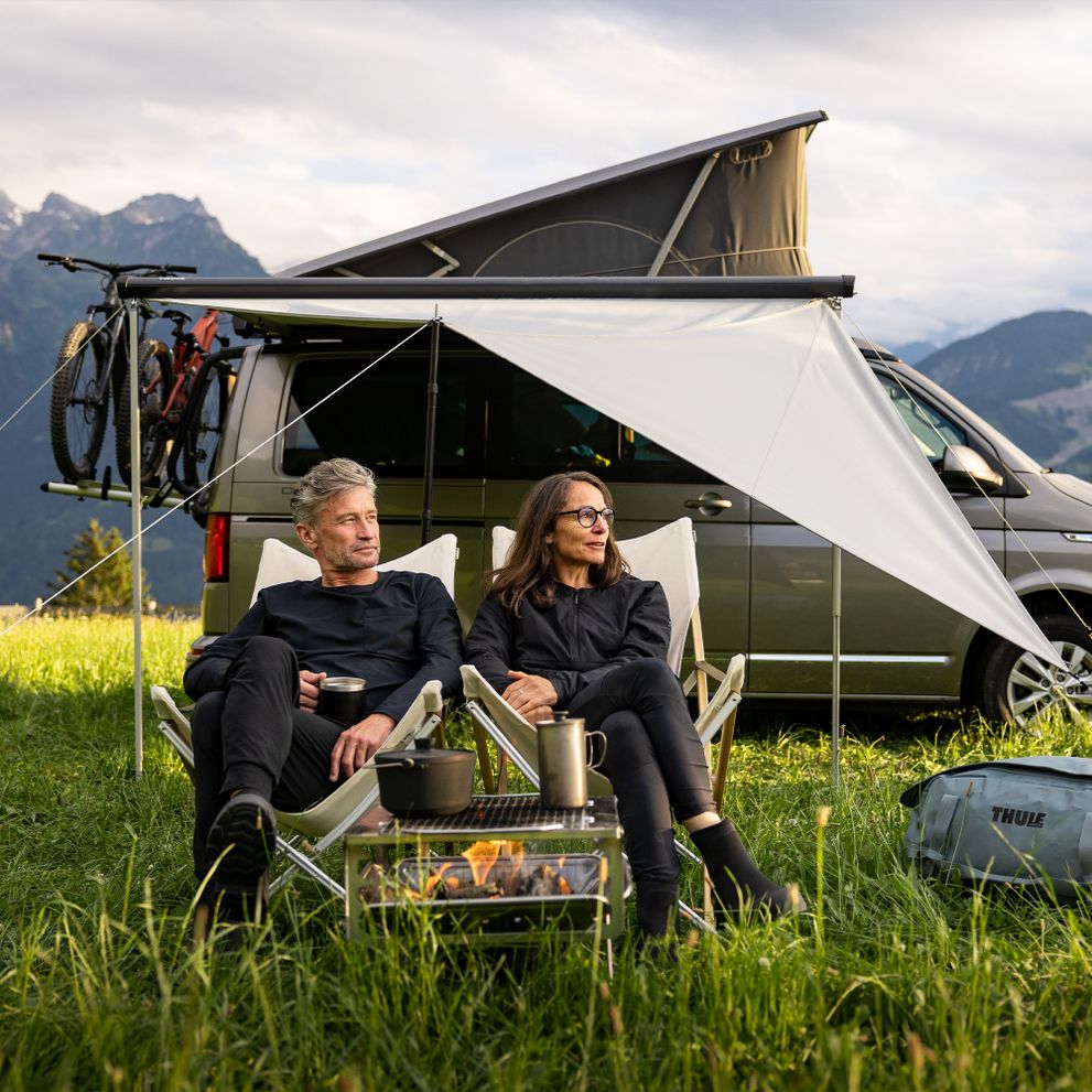 A man and a woman sit on camping chairs under the Thule Subsola van awning panels.