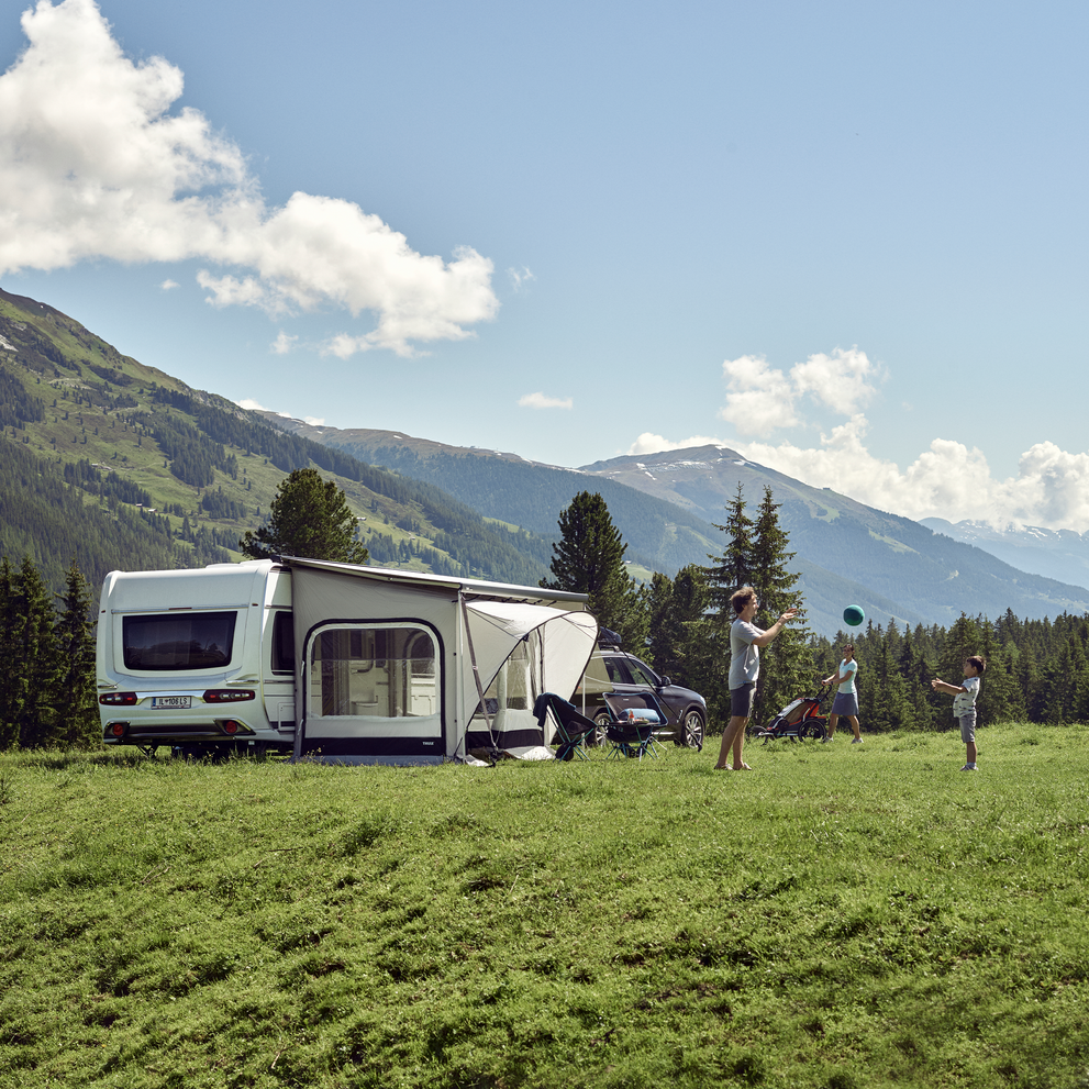 A white motorhome parked next to mountains with a Thule QuickFit rv awning tent.