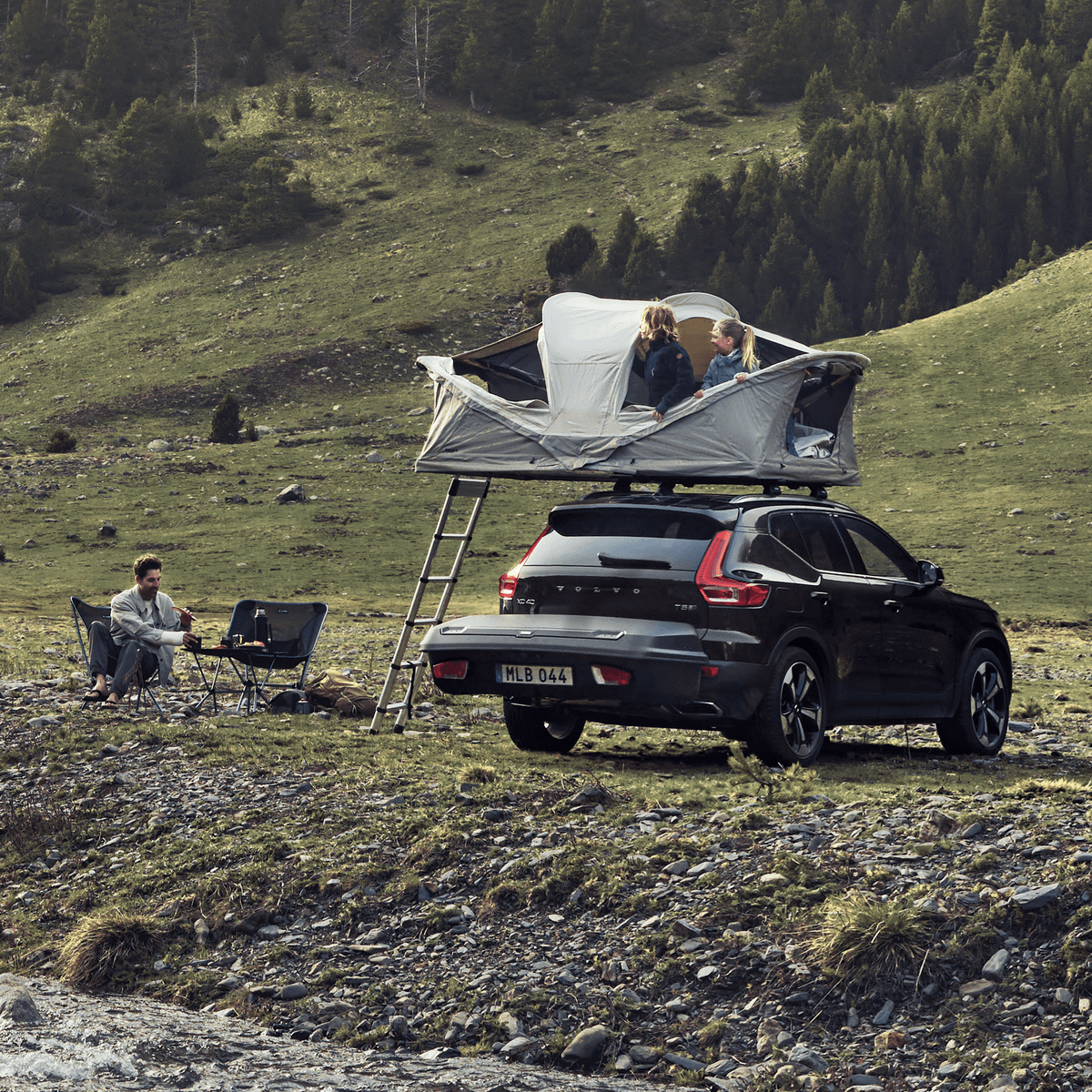 A car with a Thule Approach rooftop tent and Thule Arcos cargo box is parked outdoors.