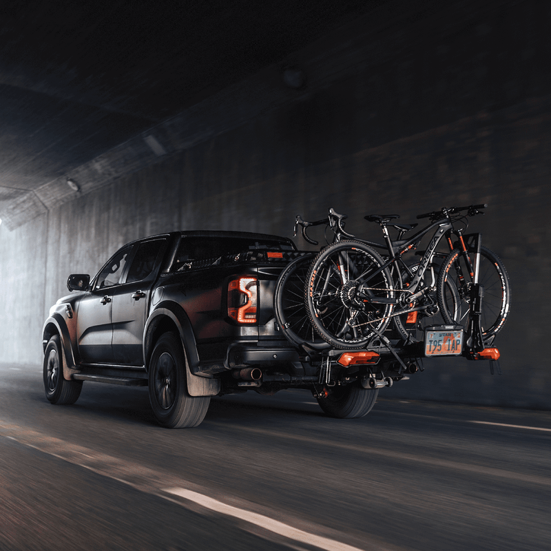 A pickup truck driving through a tunnel with two bikes mounted on a Thule Verse bike rack, equipped with Thule lights and license plate kit.