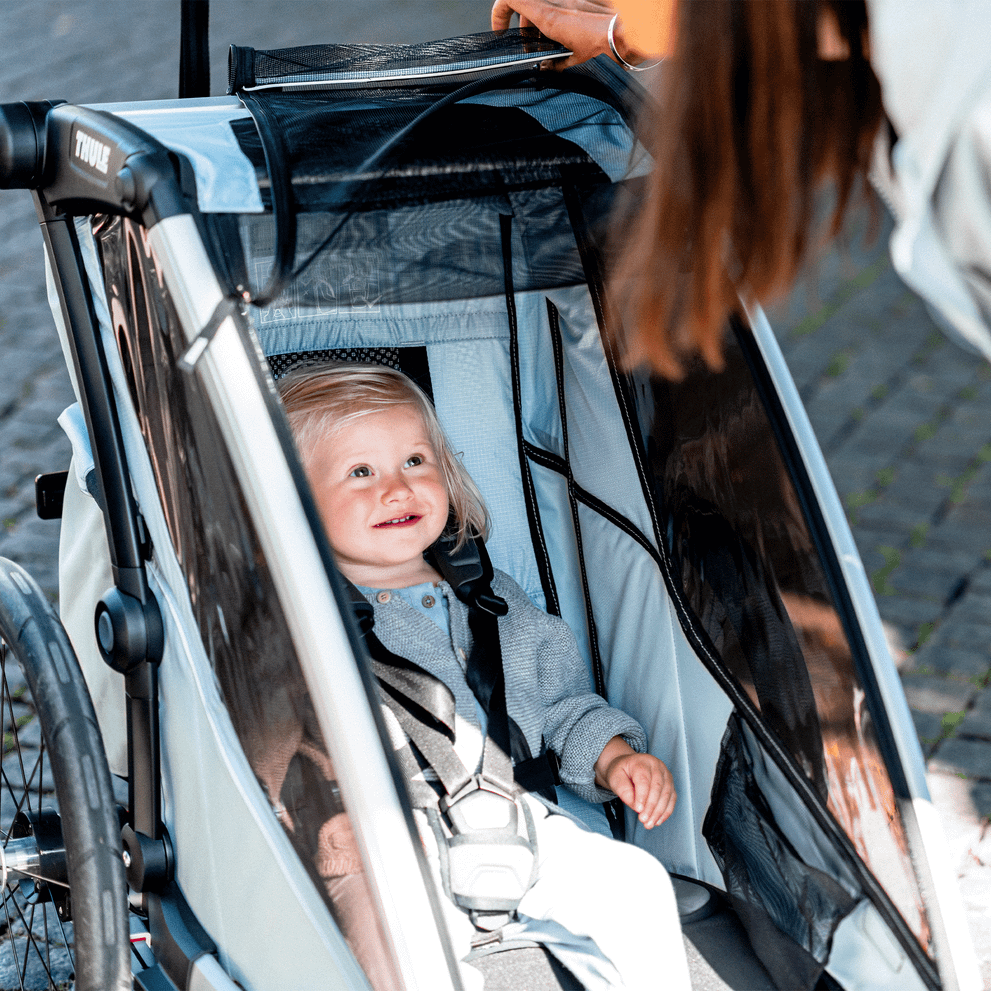 A woman looks down at her smiling child inside a blue Thule Chariot Cross.