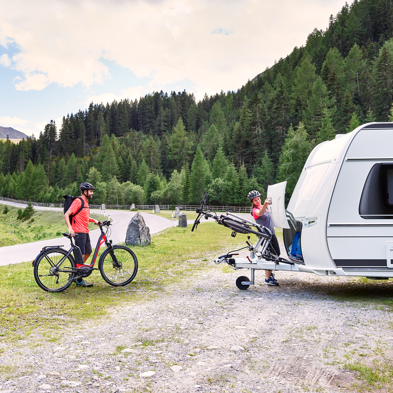 A cyclists stands next to a caravan with bikes loaded on the Thule Caravan Superb Standard caravan bike rack.