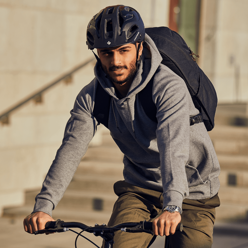 A close-up of someone sitting on a bench with a black Thule Indago backpack.