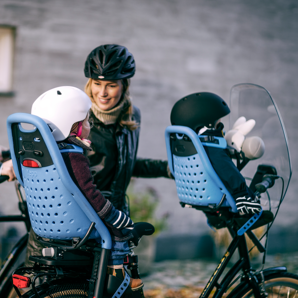 Two parents pull their bikes with kids sitting on the blue Thule Yepp Mini and Maxi child bike seats.