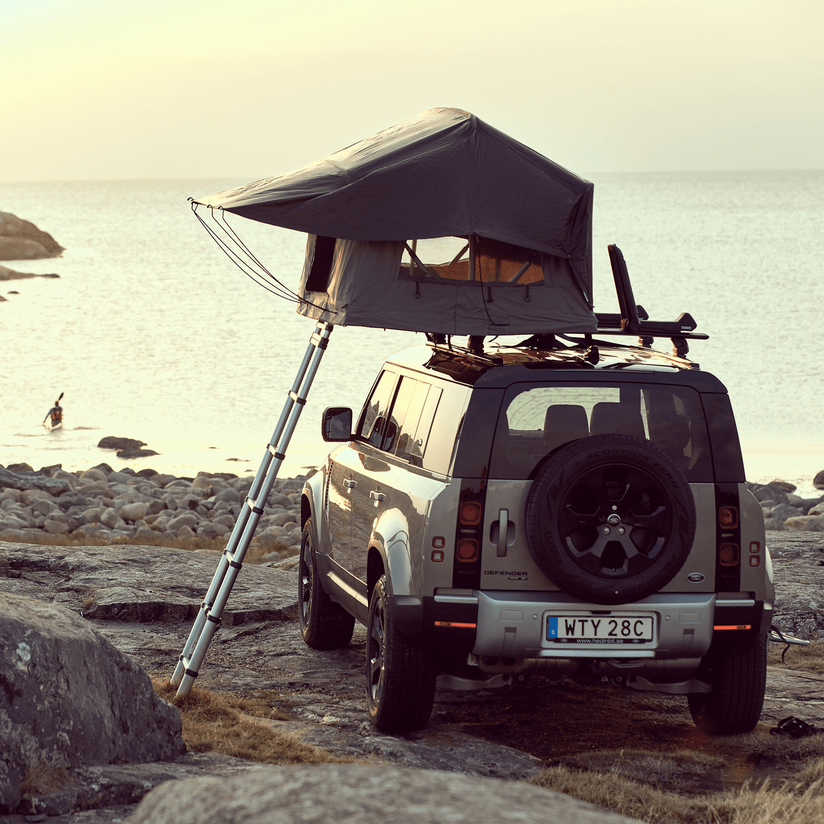 A car with a roof top tent is parked by the sea