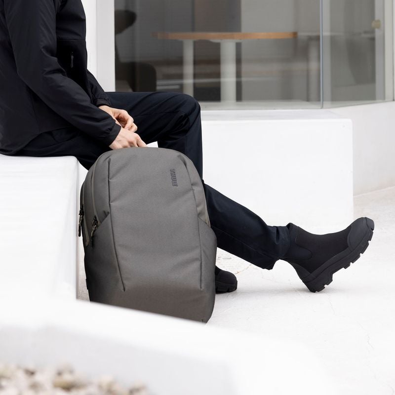 A close-up of someone sitting down wearing all black, holding Thule Subterra backpack.