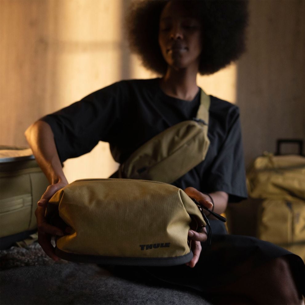 Person packing a Thule Aion toiletry bag in a hotel room.