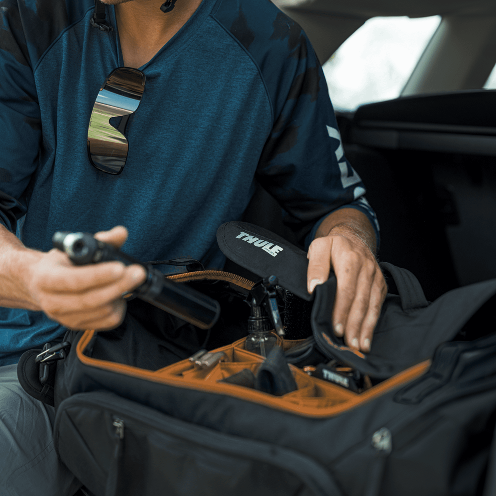 A cyclist has a Thule Roundtrip bike gear duffel in the trunk of his car and rummages for gear.