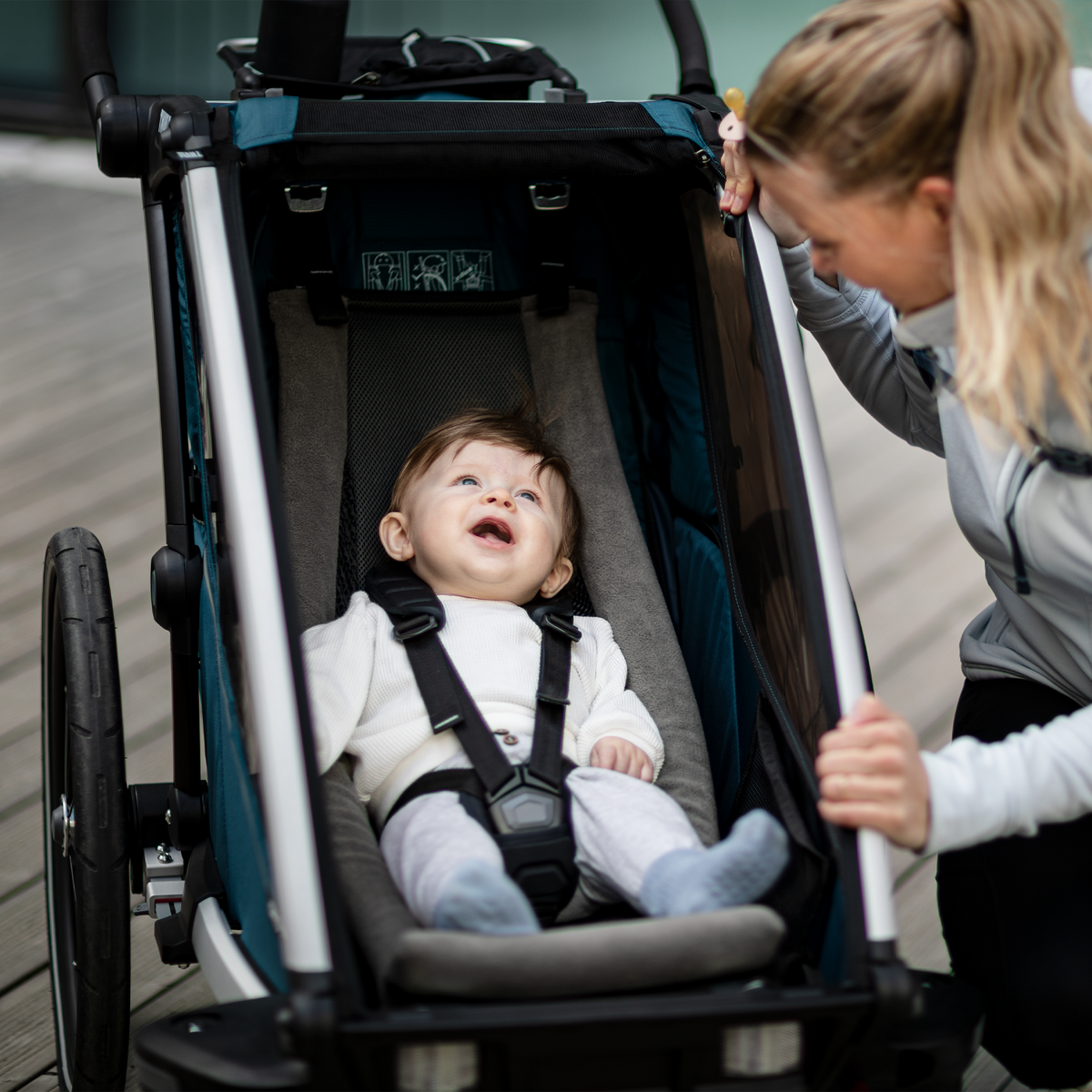 A baby sitting in a kids bike trailer with an Infant Sling looks up at her mother.