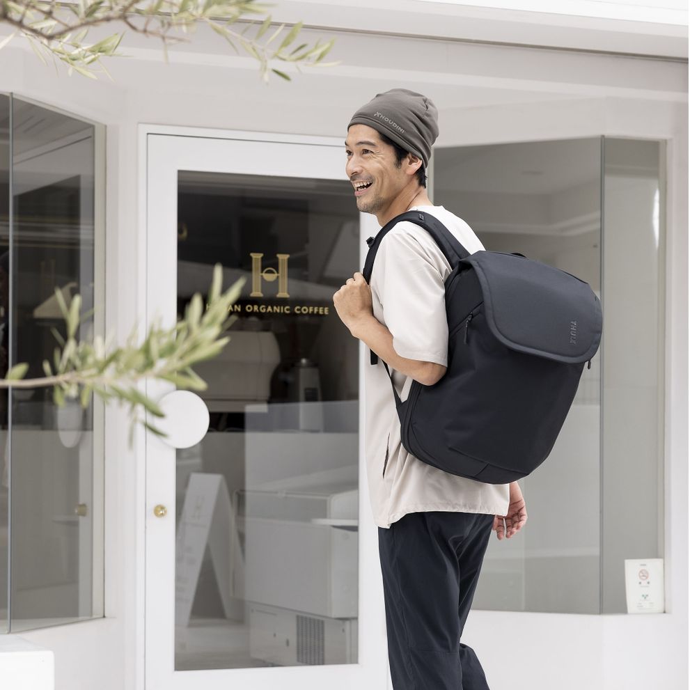 A man stands outside a white shop window with a black Thule Subterra travel backpack.