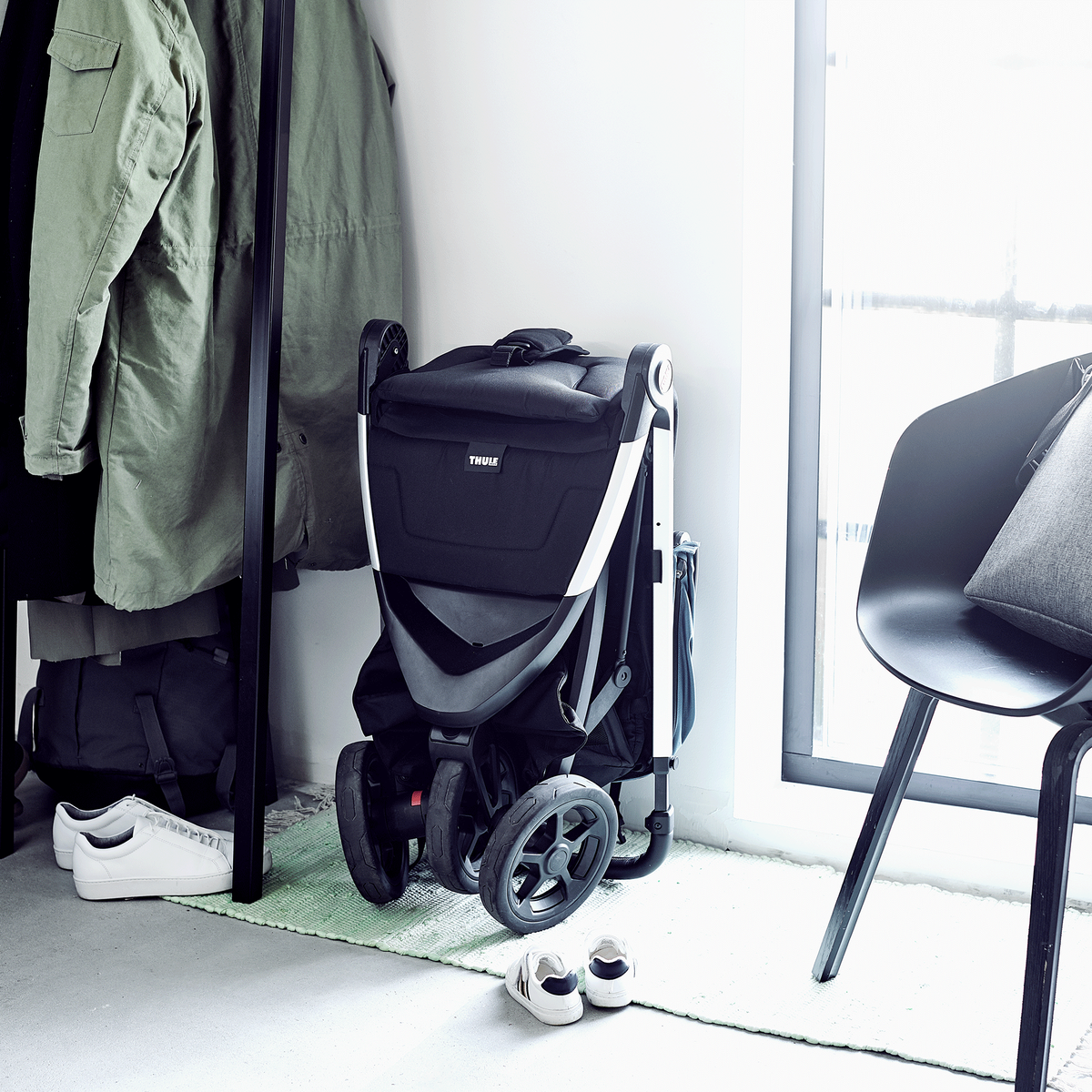 A compact Thule Spring stroller is folded and stored away beside a clothing rack and chair.
