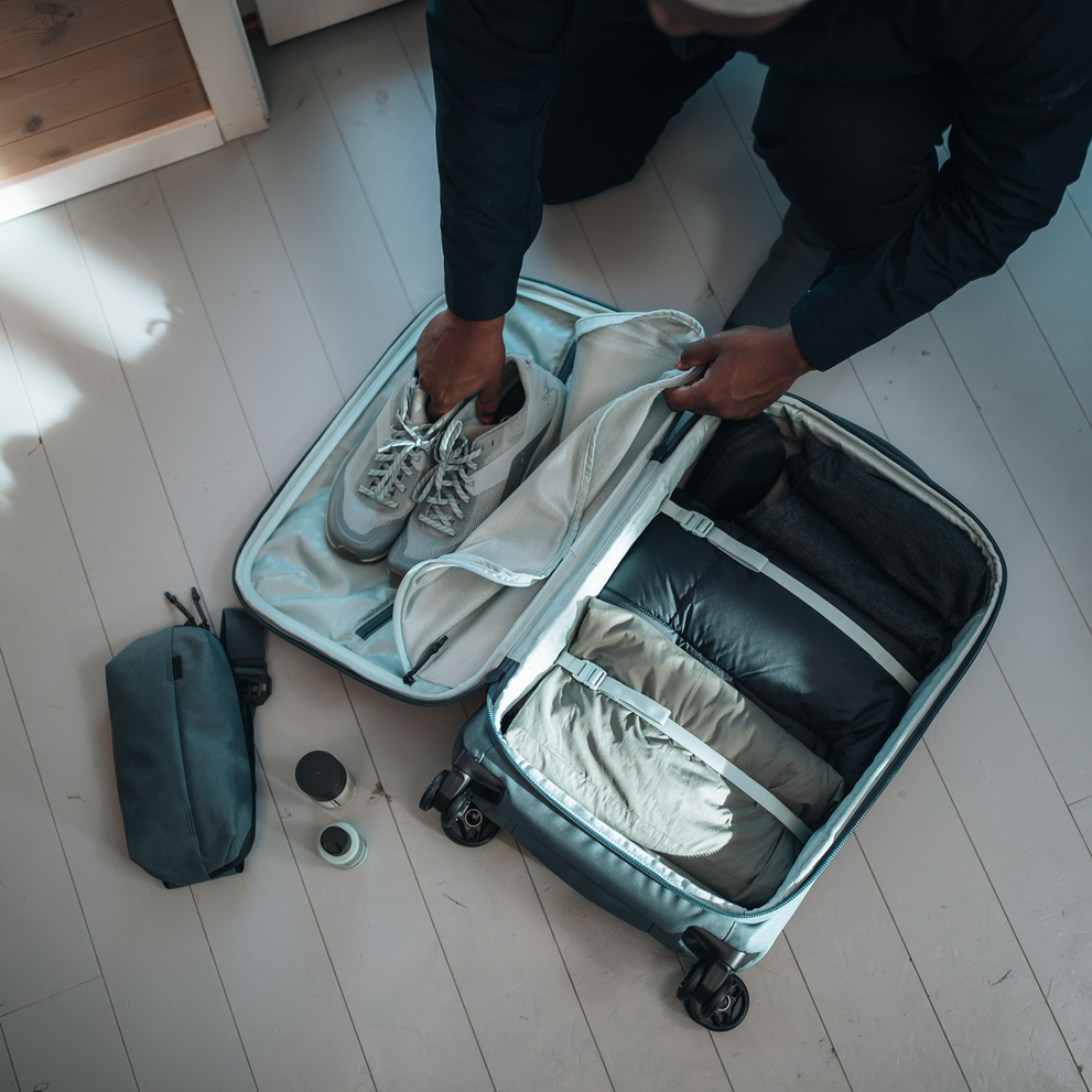 A person loads their Thule Aion carry-on suitcase with shoes, clothes, and other items.