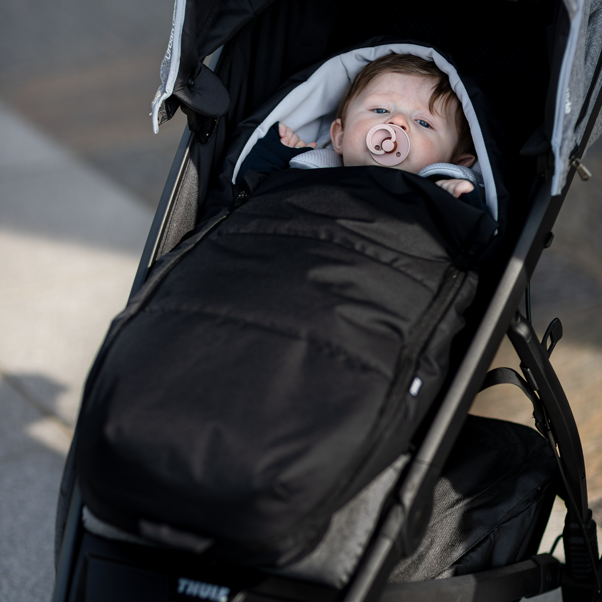 A toddler sits with a pacifier bundled in aThule Newborn Nest for Thule strollers.