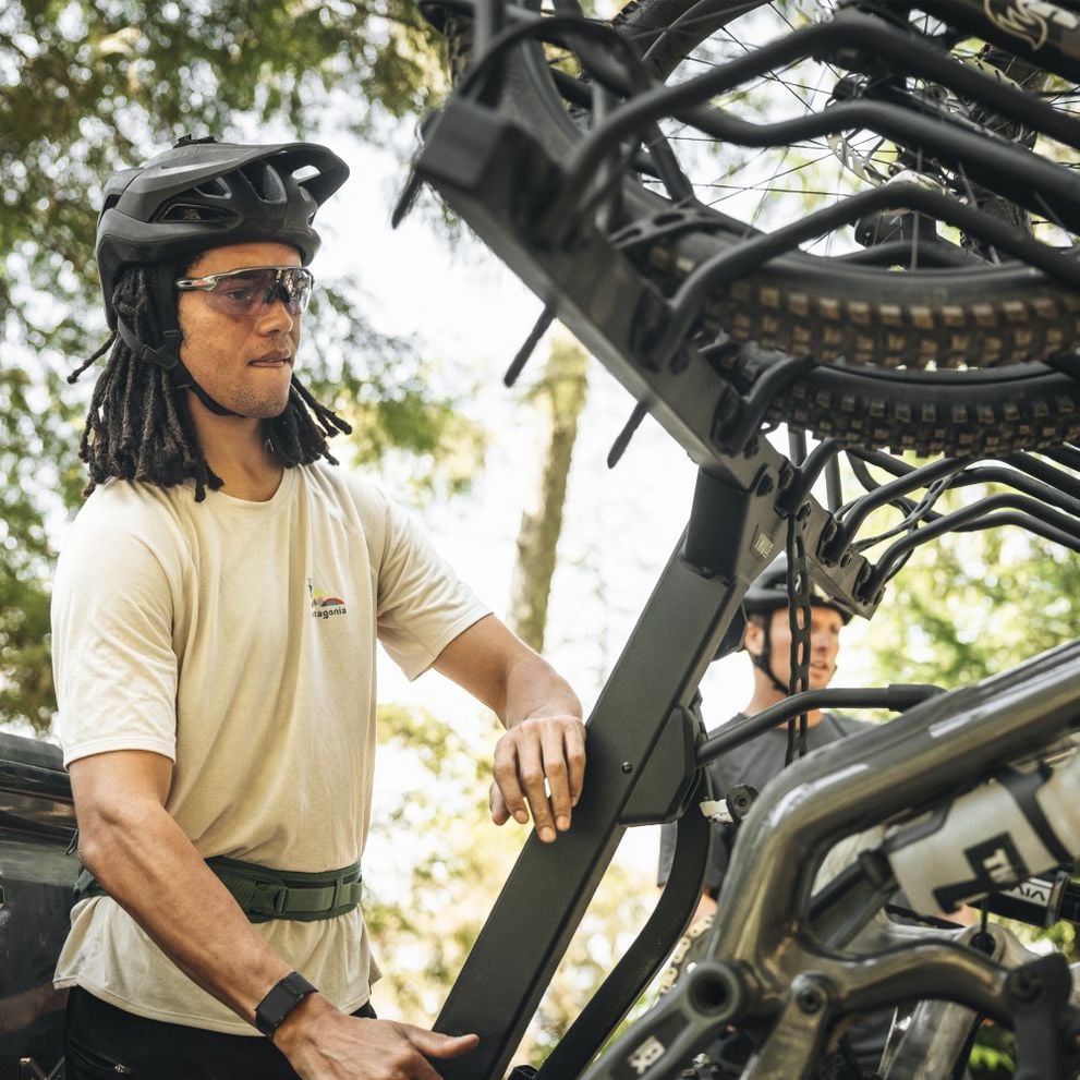 A man in a bike helmet is operating the vertical Thule ReVert hitch bike rack.