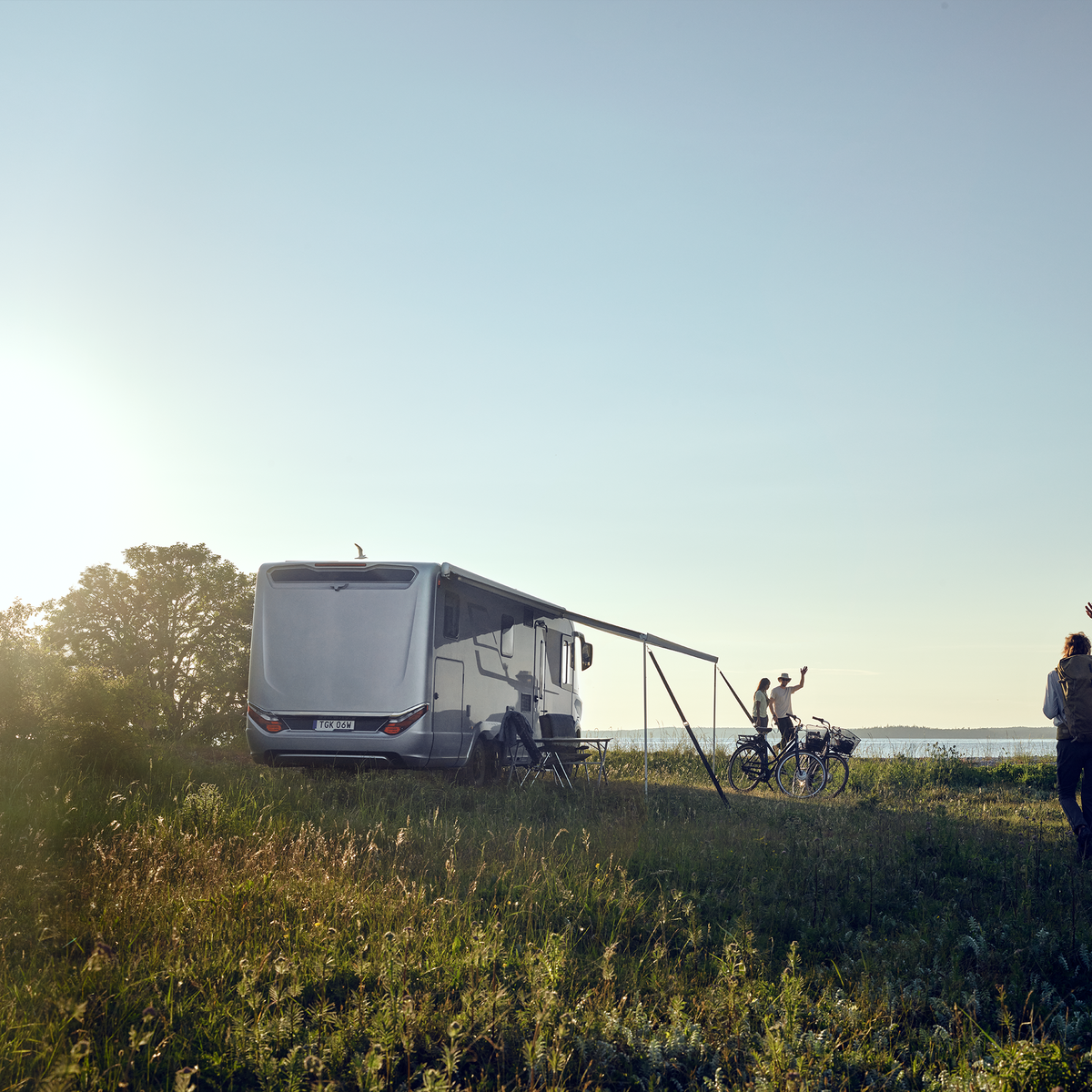 Two people wave to a couple sitting under their Thule Omnistor 8000 RV awning.
