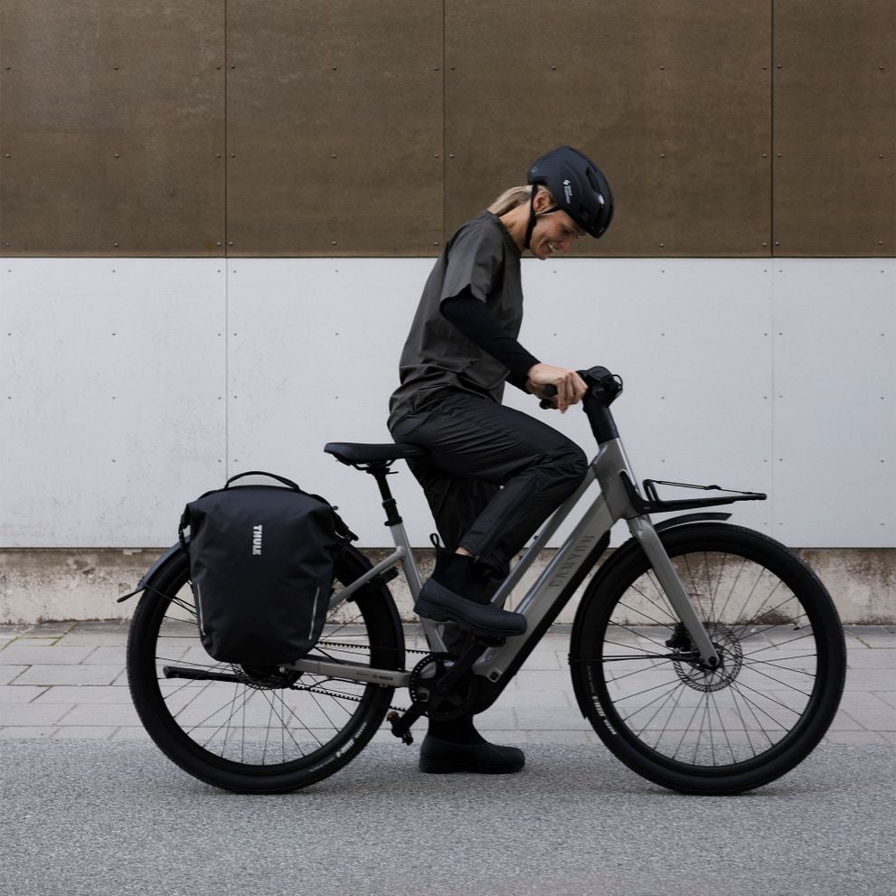 Cyclist adjusting a bike with a Thule Shield bag mounted on the rear rack.