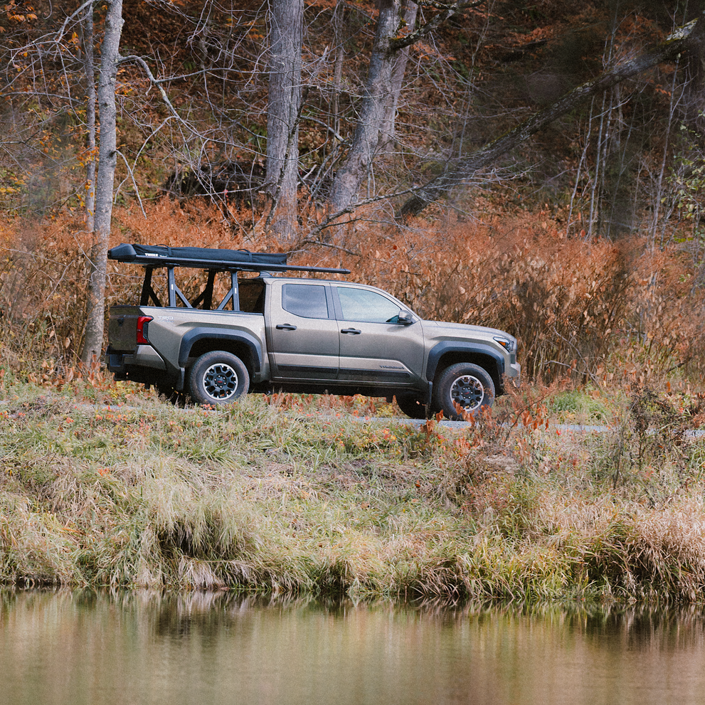 A vehicle with the Thule Xscape truck rack that carries the rooftop tent Thule Foothill and the fishing rod rack Thule RodVault 2 in an outdoors environment.