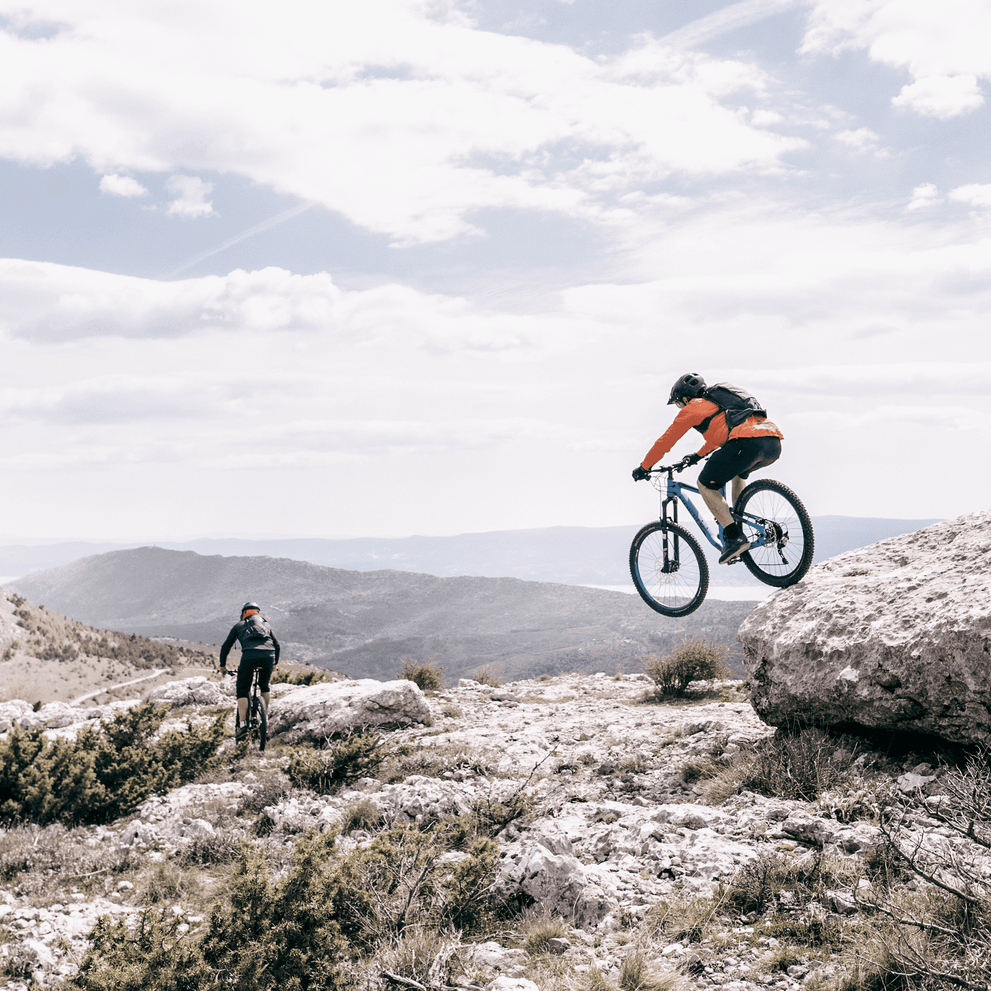 Two people go mountain biking in a rocky trail with a Thule Vital hydration backpack.