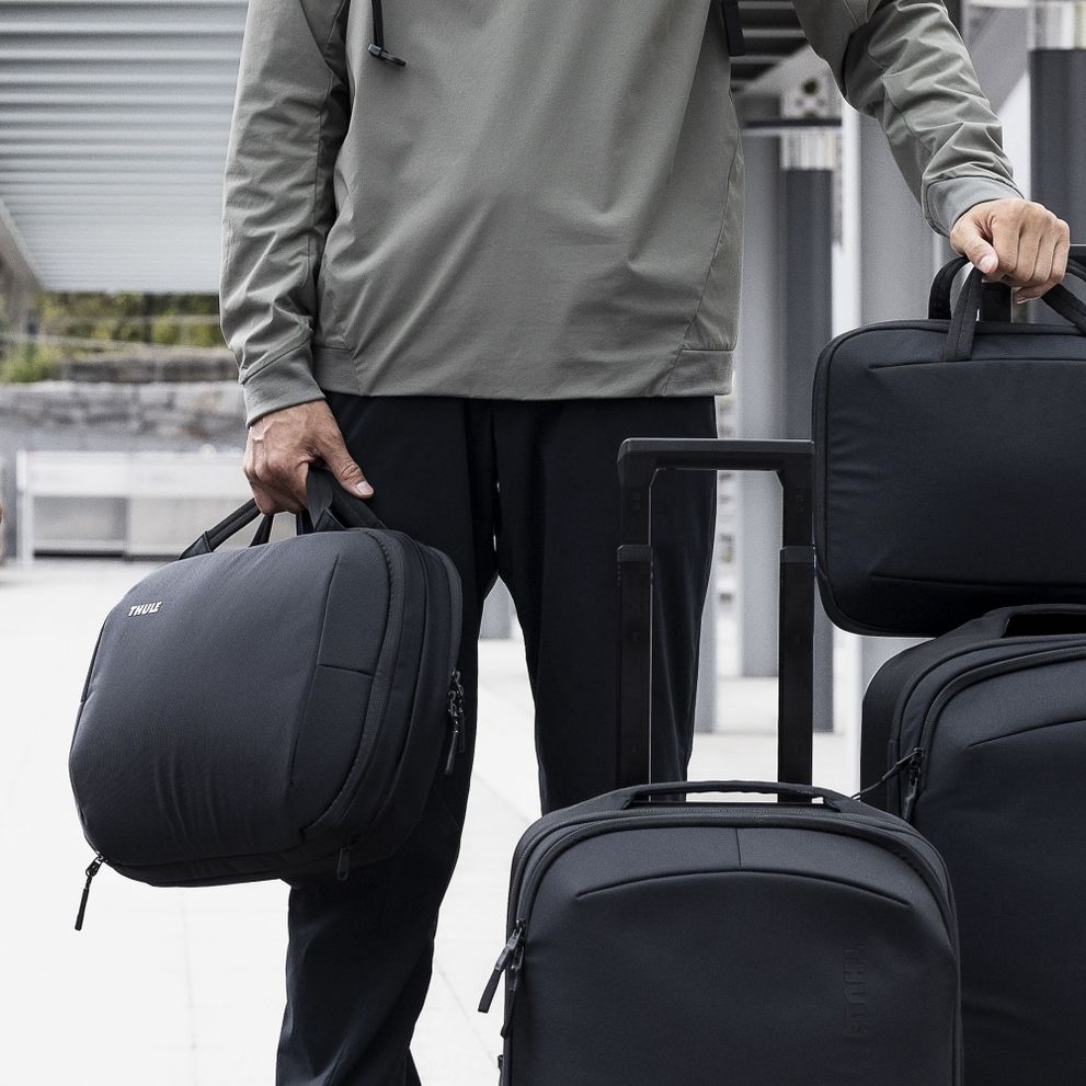 A close-up of a man holding black Thule Subterra luggage.
