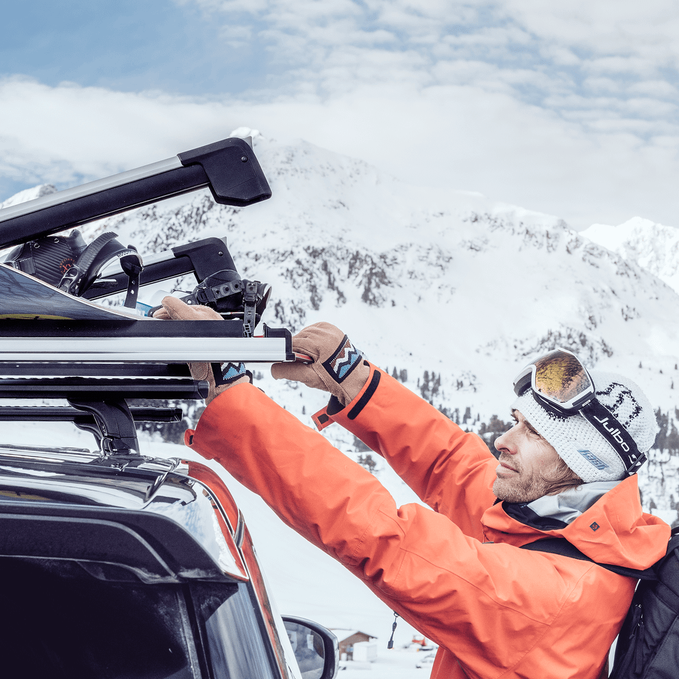A man is fastening his snowboard on a car roof with a Thule SnowPack Extender