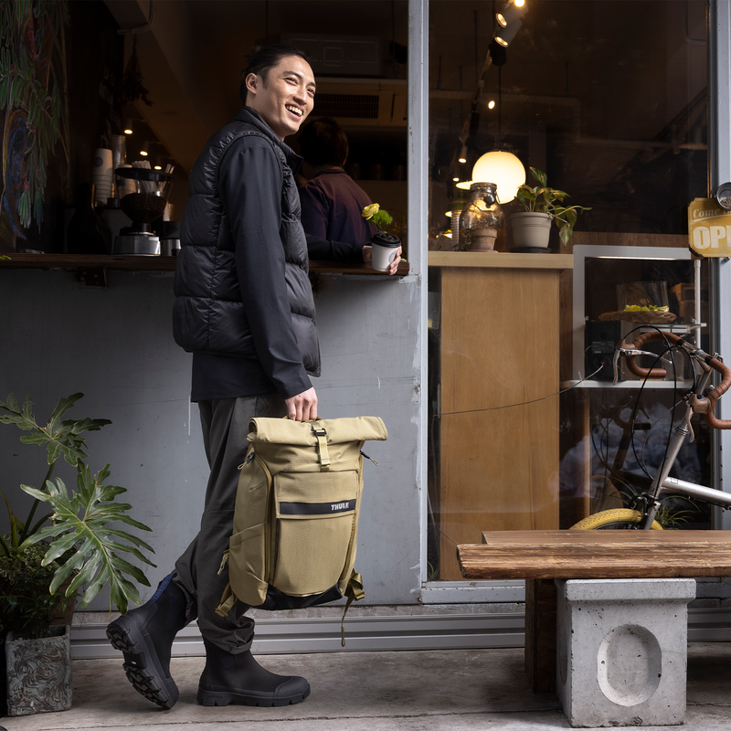 Man outside cafe holding the Thule Paramount backpack 24L