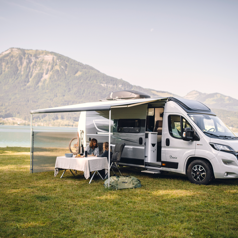 An rv parked next to a lake and a mountain with an awning and a Thule View Blocker Side awning side wall.