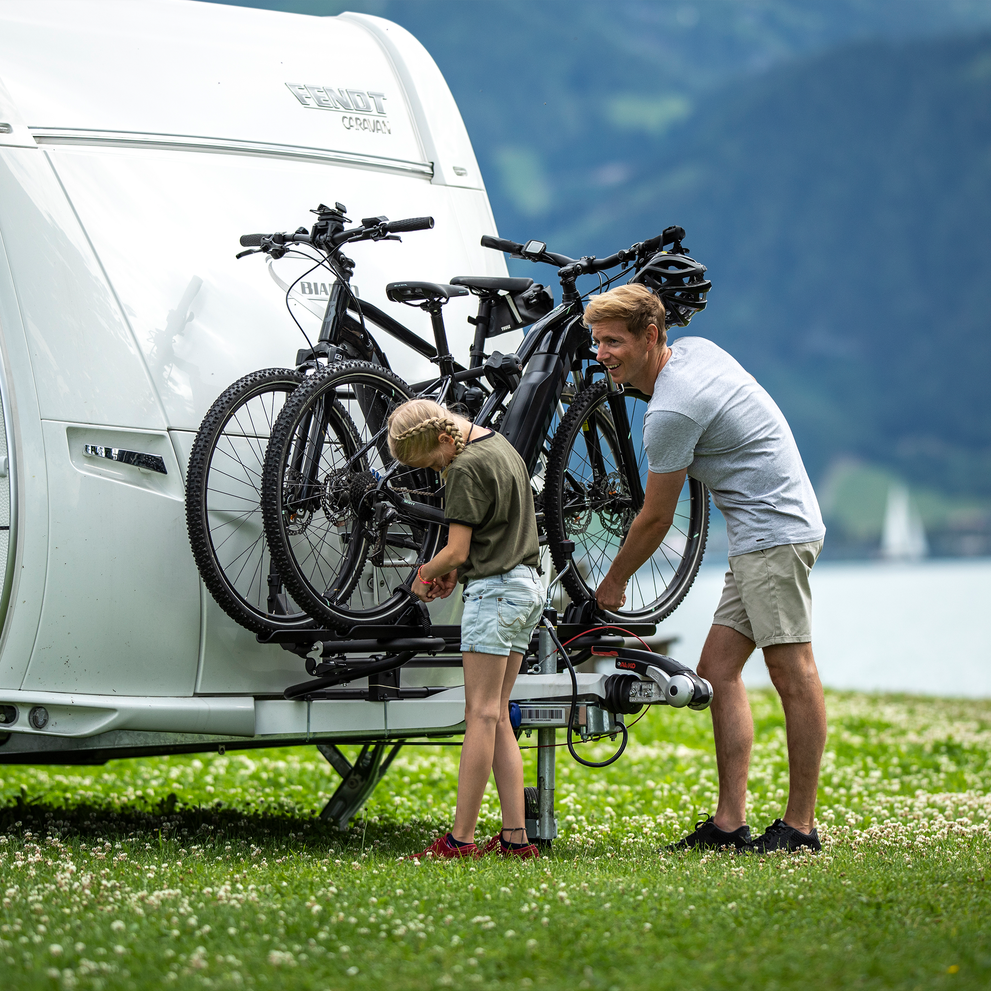 A man unloads bikes from a Thule Caravan Superb XT caravan bike rack looking at his child.