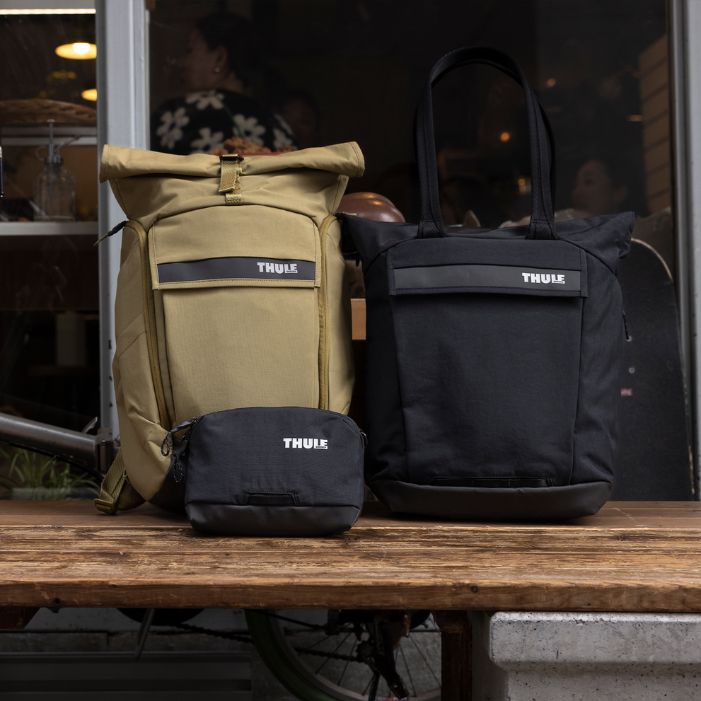 Three bags including Thule Paramount 2L crossbody bag are leaning against a bike.