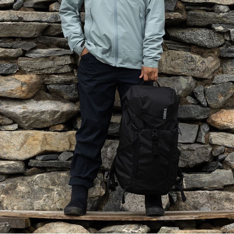 A close-up of a woman holding a black Thule AllTrail hiking backpack.