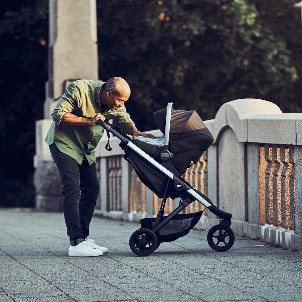 On a park bridge, a man tends to his baby in a car seat using the Thule Spring Car Seat Adapter.