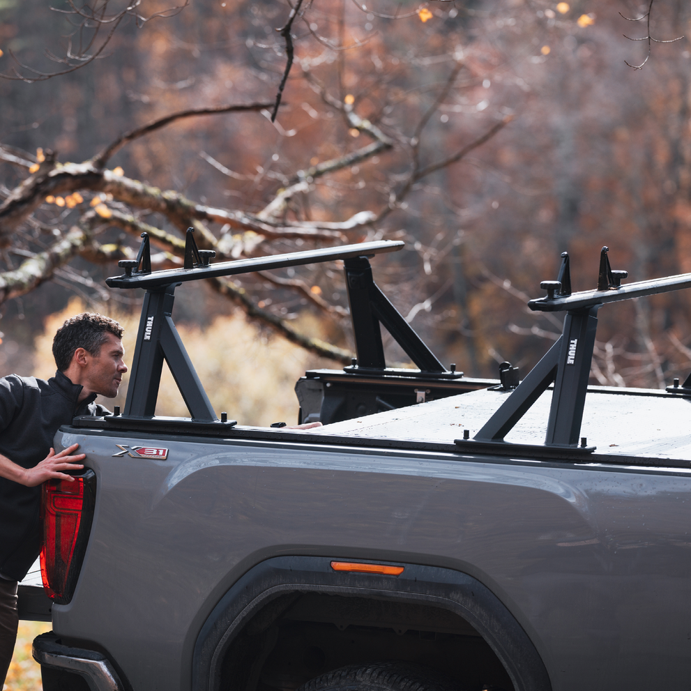 A man stands behind a vehicle with the Thule Xscape truck rack in an outdoors environment.