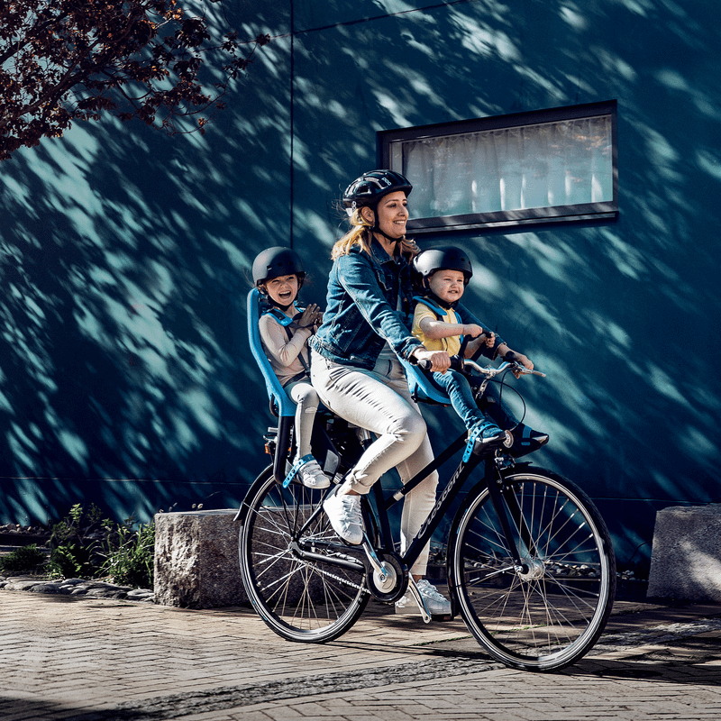 A woman bikes down a street with a cherry tree, with her baby in a Thule Yepp Mini child bike seat.