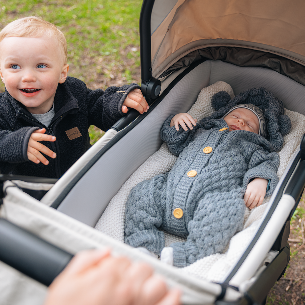 Baby lying in Thule Spring 2 bassinet while sibling smiles nearby.